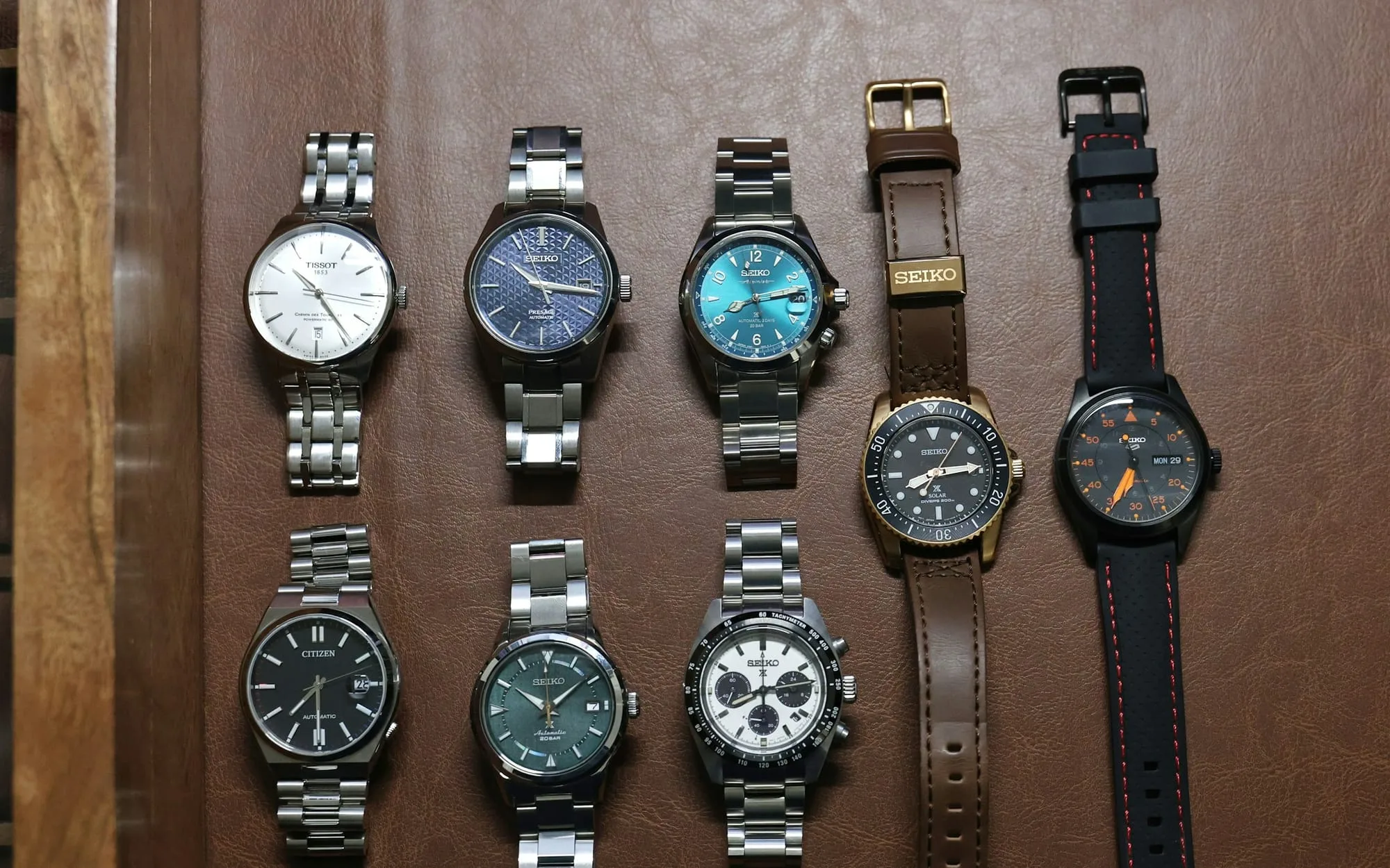 Eight steel sports watches laid out in two rows on a wooden case