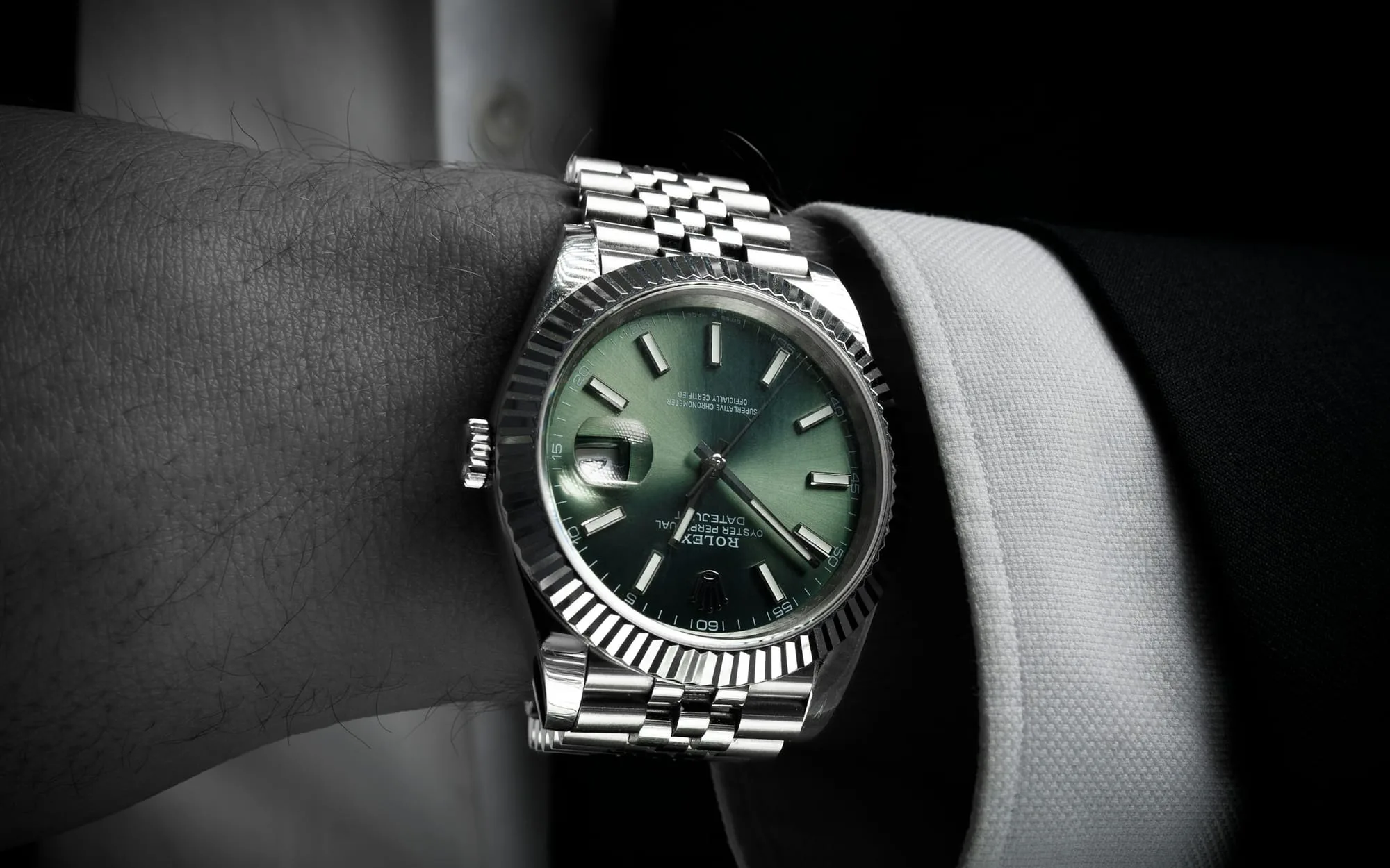 A green-dial Rolex on the wrist of a man in a dark suit