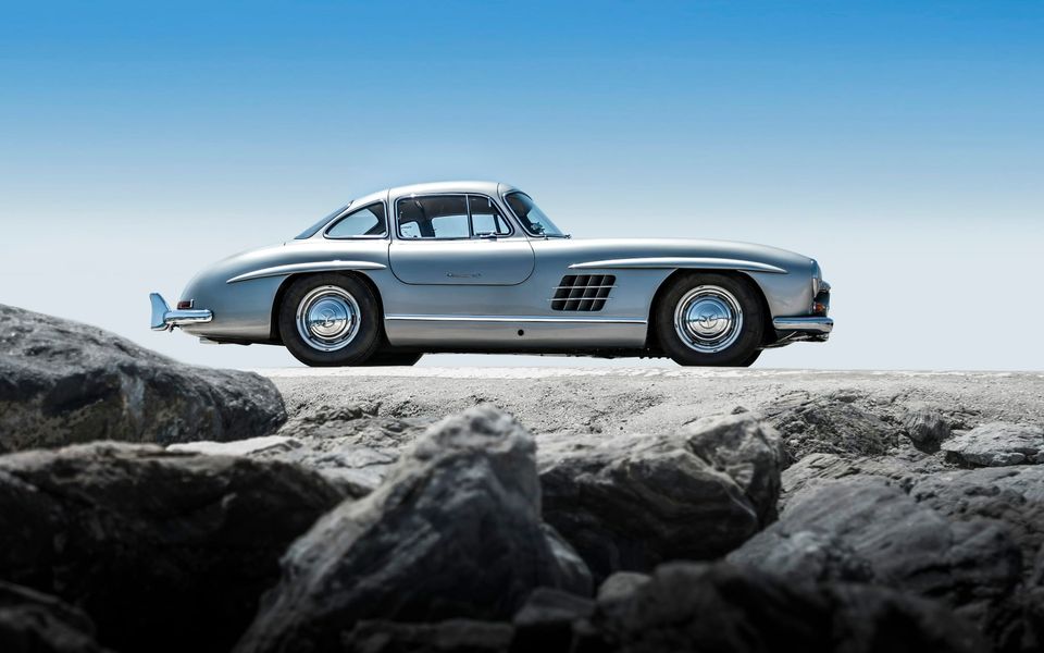 A silver Mercedes-Benz 300 SL Gullwing on a rocky shore