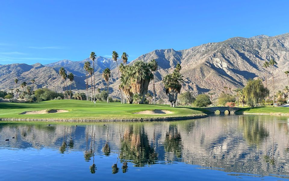 A desert golf course with a lake, palms and mountains