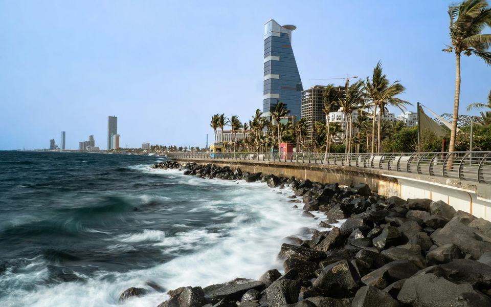 Waves breaking on the rocks of the Jeddah Corniche, with towers behind