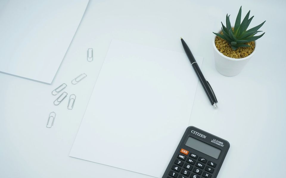 Blank document, pen, paper clips and a calculator on a white desk