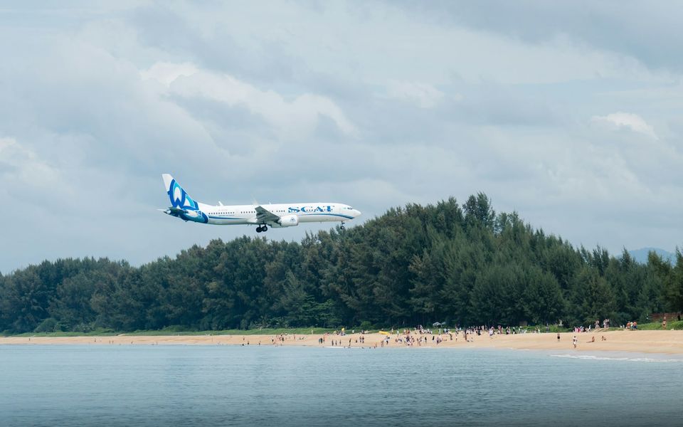 A passenger jet on final approach over Mai Khao Beach, with plane-spotters on the sand