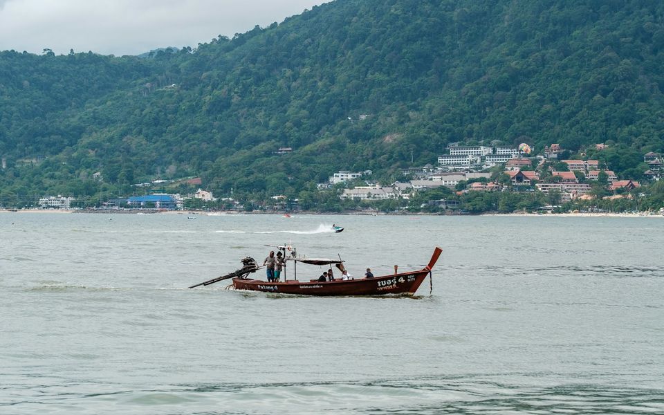 A longtail boat marked 'Patong 4' crossing Patong Bay, with Kalim hillside resorts behind