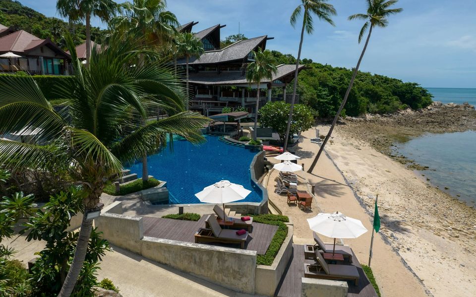 Beachfront resort pool with sun loungers and parasols beneath Thai-style roofs