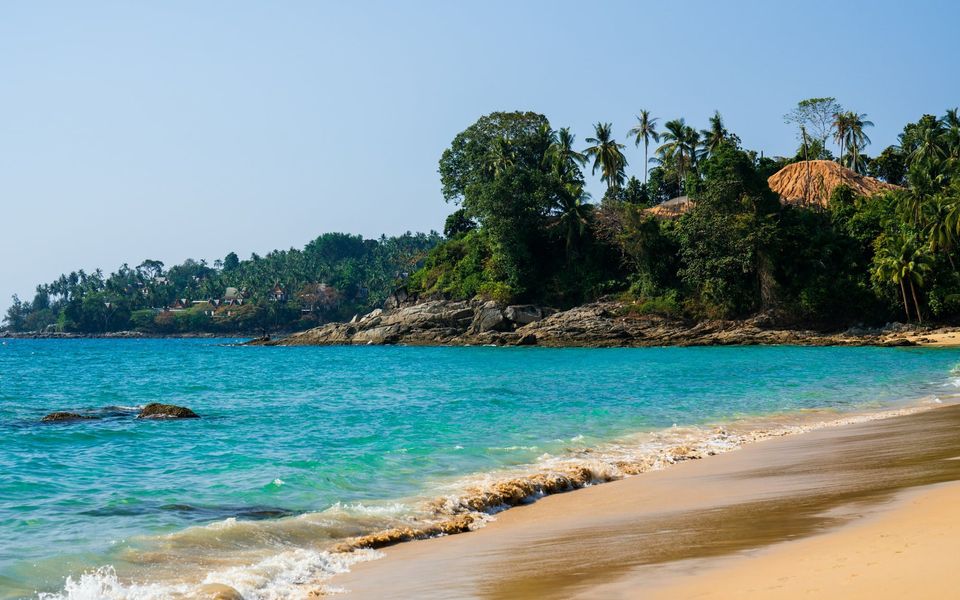 Turquoise water and the rocky north headland of Surin Beach, with villas among the palms